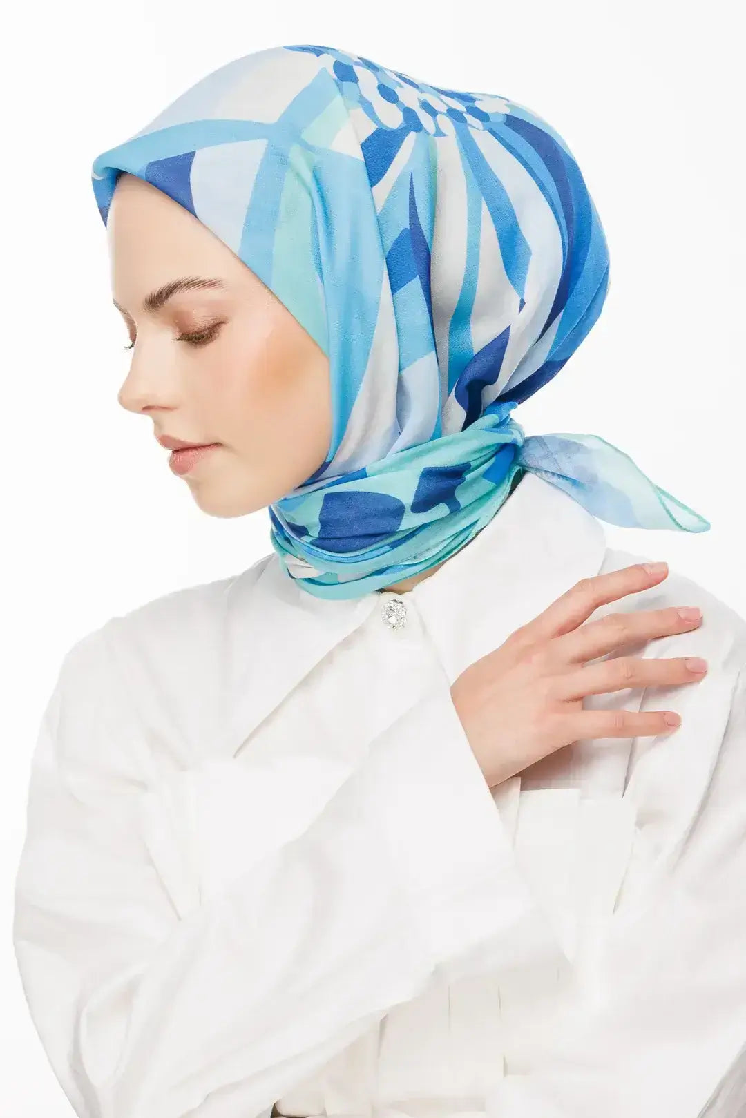 "Flora Eşarp Koleksiyonu - Geometrik desenli mavi tonlarında tasarlanmış Flora eşarp, beyaz gömlekli model üzerinde zarif bir duruşla sergileniyor."