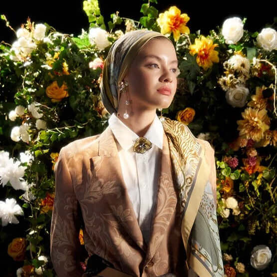 "Çiçeklerle süslenmiş fonda etnik desenli şal ve klasik ceket kombiniyle zarif bir poz veren kadın model"