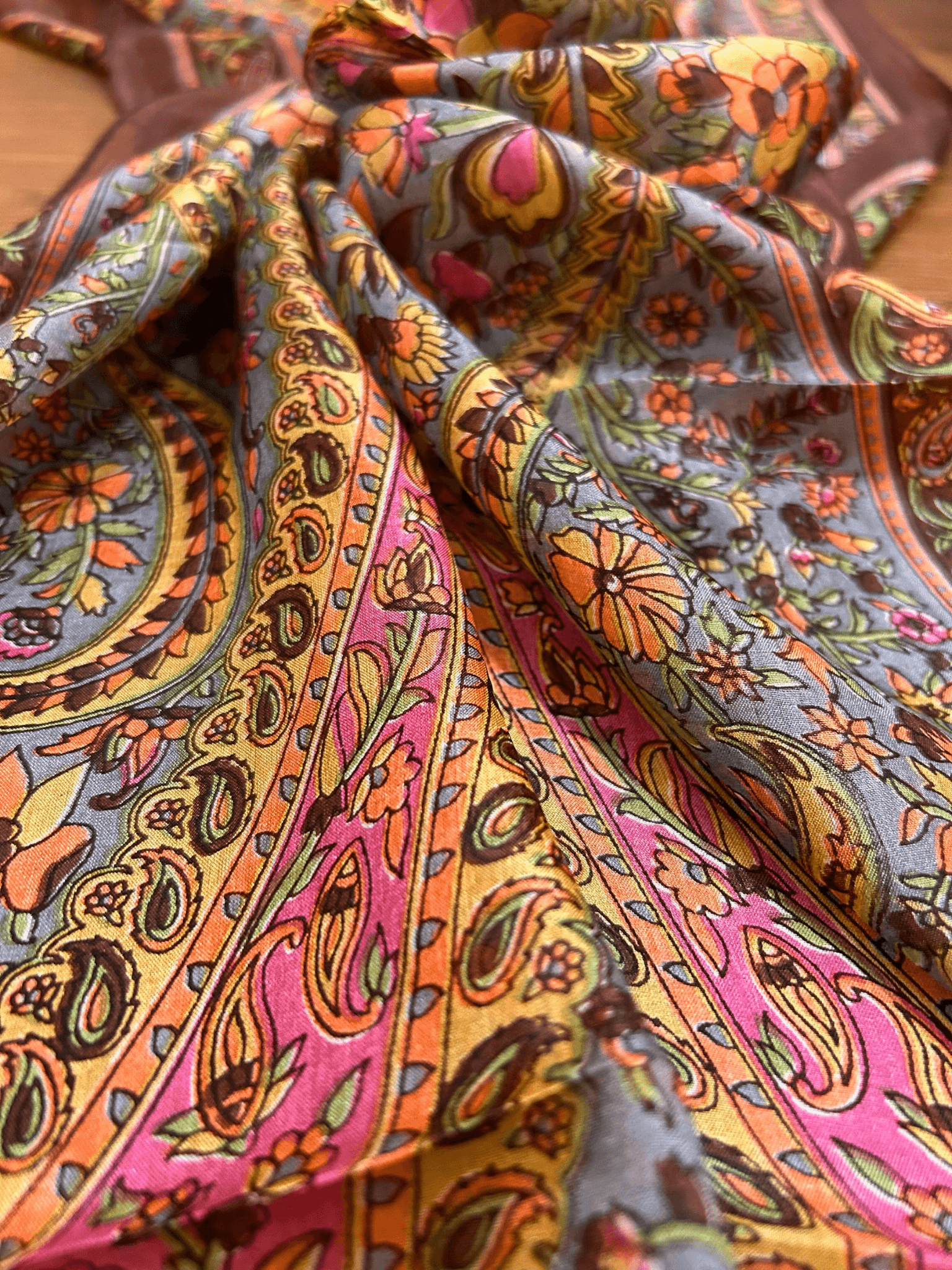 "Kahverengi kenarlı, pembe, sarı ve mavi tonlarında paisley ve floral desenli Hint ipeği fular – sıcak renk geçişleriyle klasik ve zarif bir görünüm sunar."
