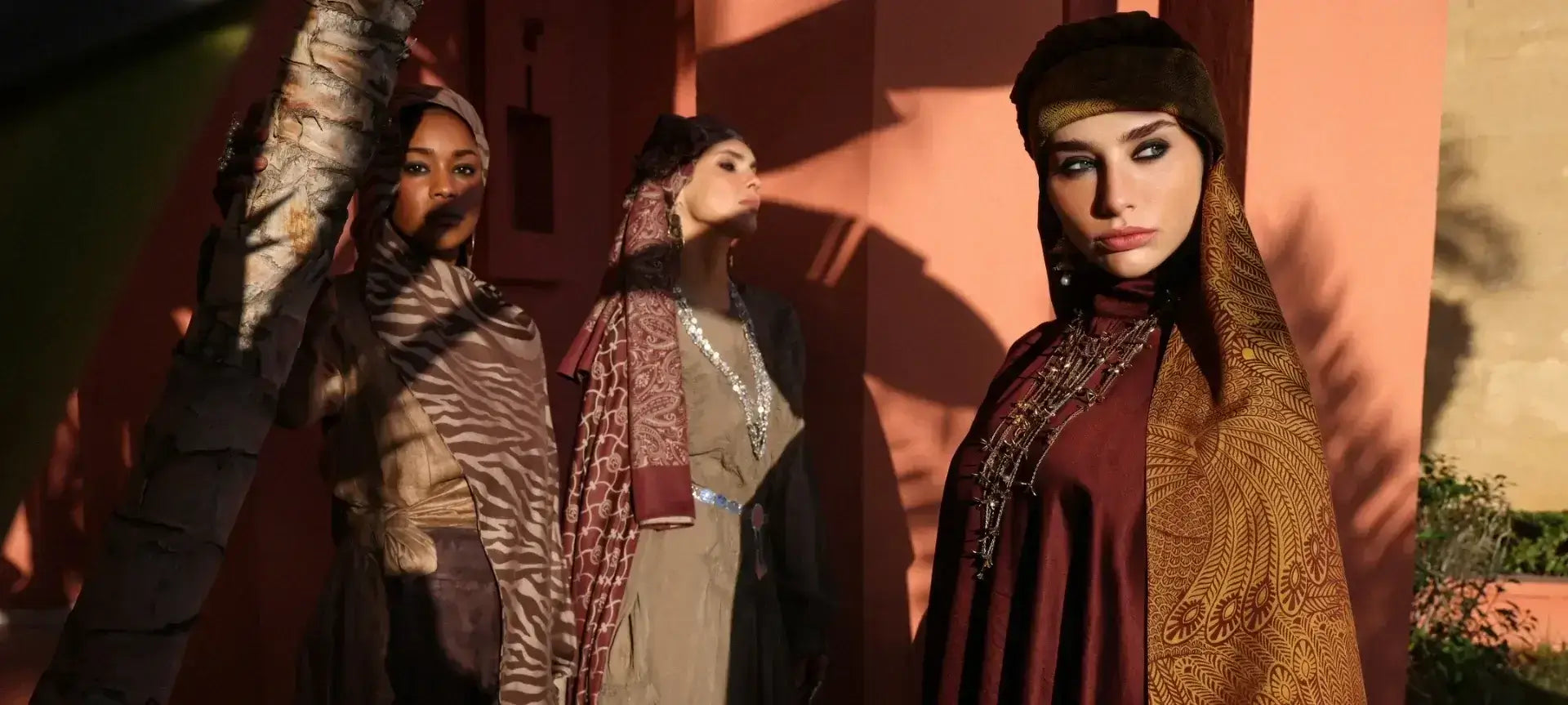 "Marrakech Koleksiyonu'na ait etnik desenli kahverengi, bordo ve zebra desenli şallar; sıcak tonlu Fas mimarisi önünde üç farklı model üzerinde sergileniyor."