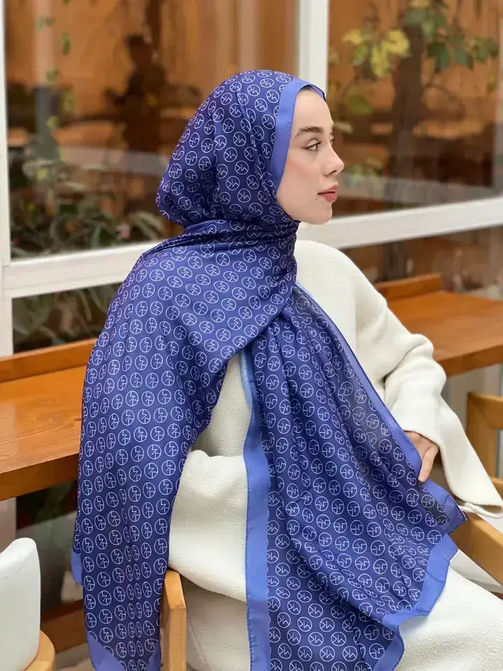MK desenli mor mavi şal takan kadın model, iç mekanda otururken yandan bakış