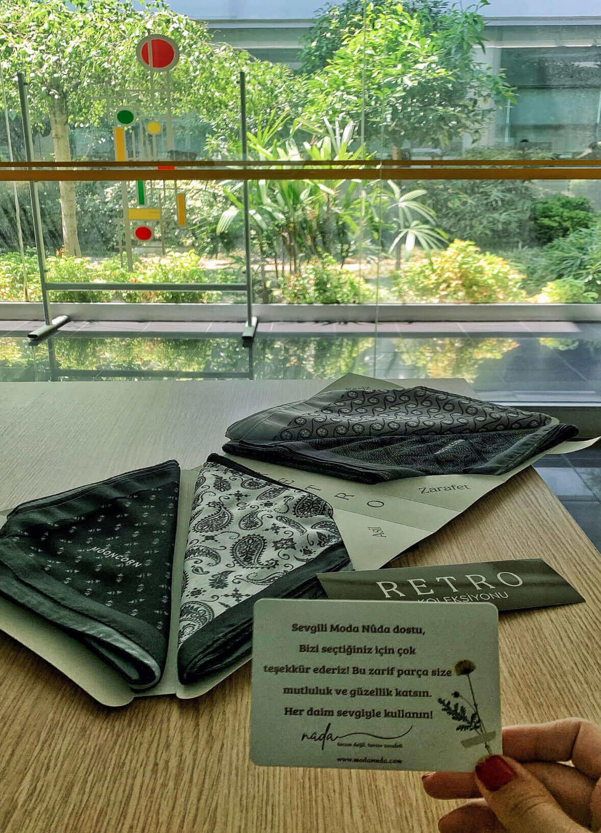 "Moda Nûda Retro Koleksiyonu siyah beyaz desenli fular seti – masa üstünde doğayla iç içe bir ortamda sunulmuş hediye paketiyle birlikte"