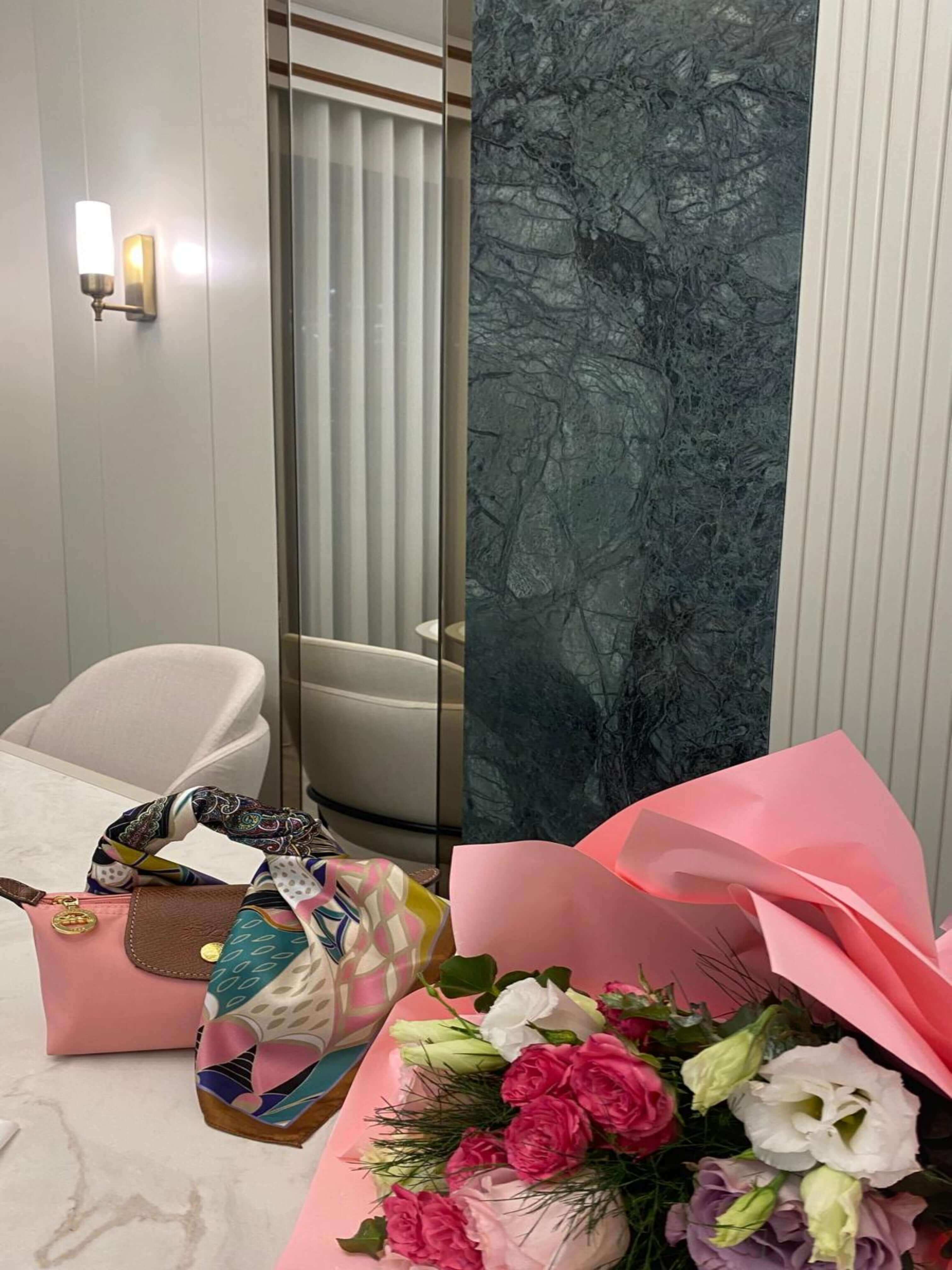 "Moda Nûda Solena fular koleksiyonu – pembe çanta sapına sarılmış renkli desenli ipek fular ve çiçek buketiyle şık masa dekorasyonu"