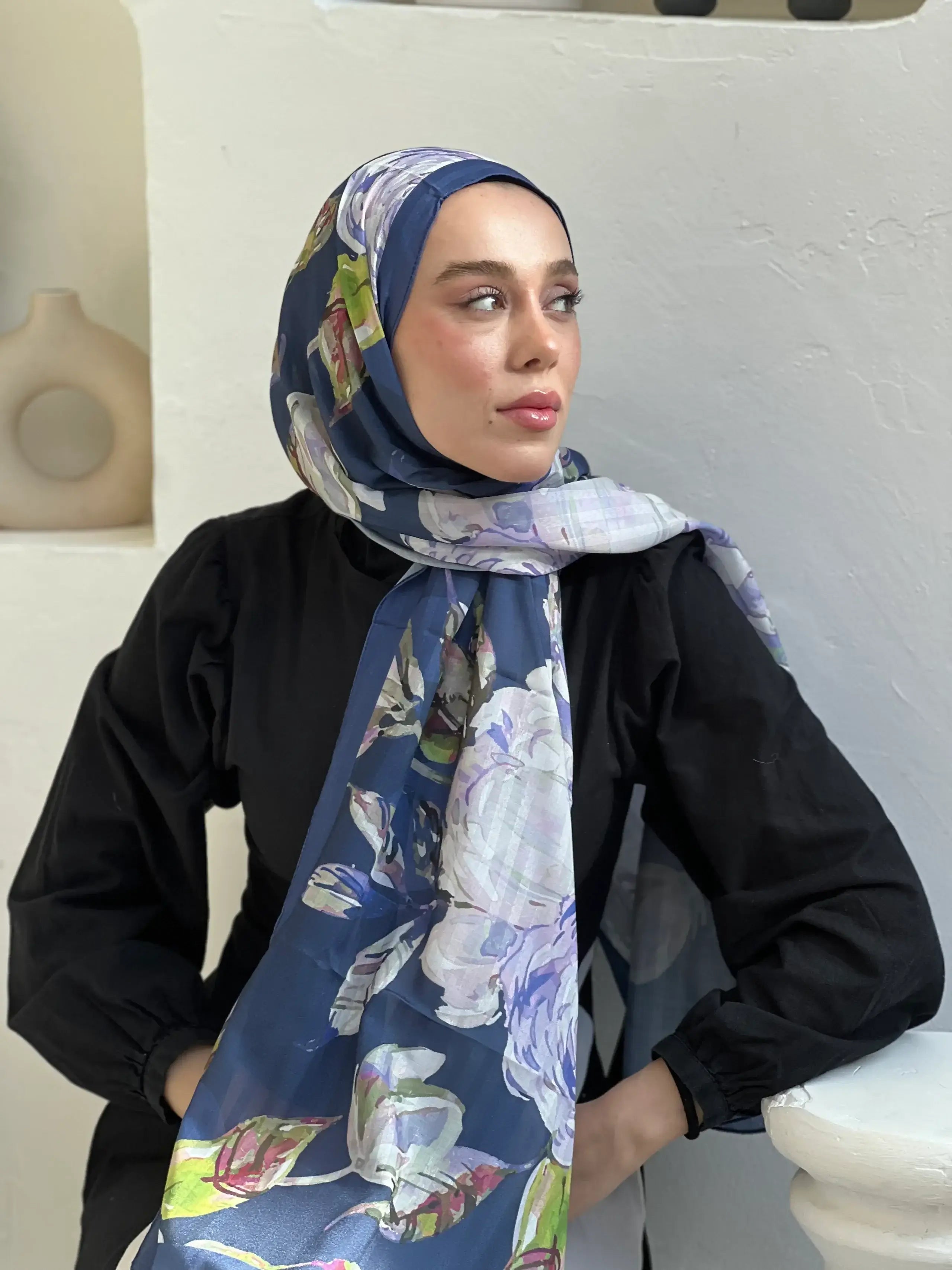 "Gece mavisi zemin üzerine pastel tonlarda çiçek desenli Acelya şal – siyah kombinle tamamlanmış zarif ve modern başörtüsü stili."
